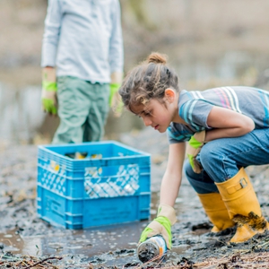 young child picking up trash along a stream